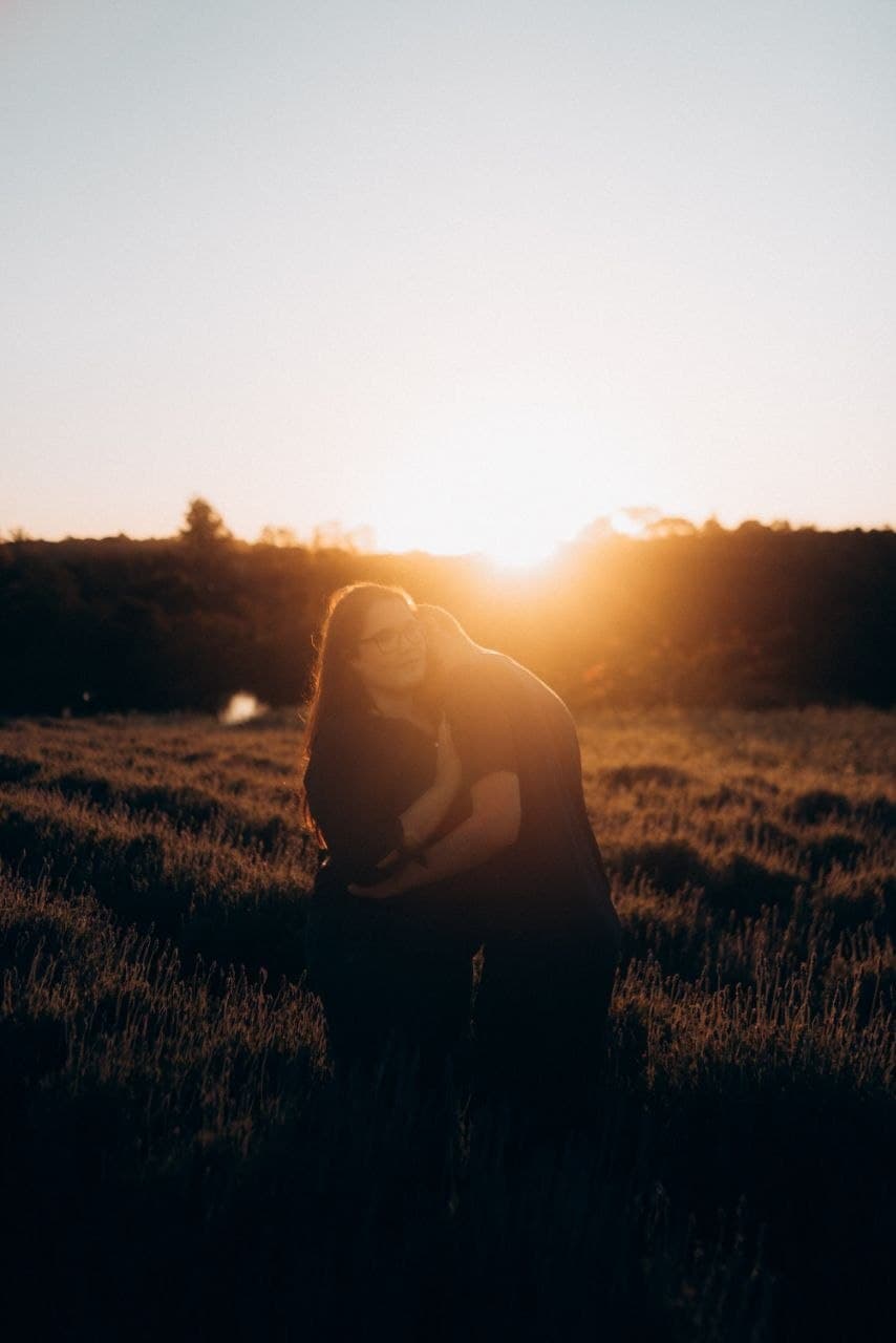 Camila e Bernardo abraçados ao pôr do sol em um campo