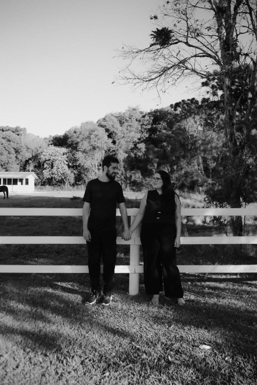 Camila e Bernardo de mãos dadas junto a uma cerca em uma fotografia em preto e branco