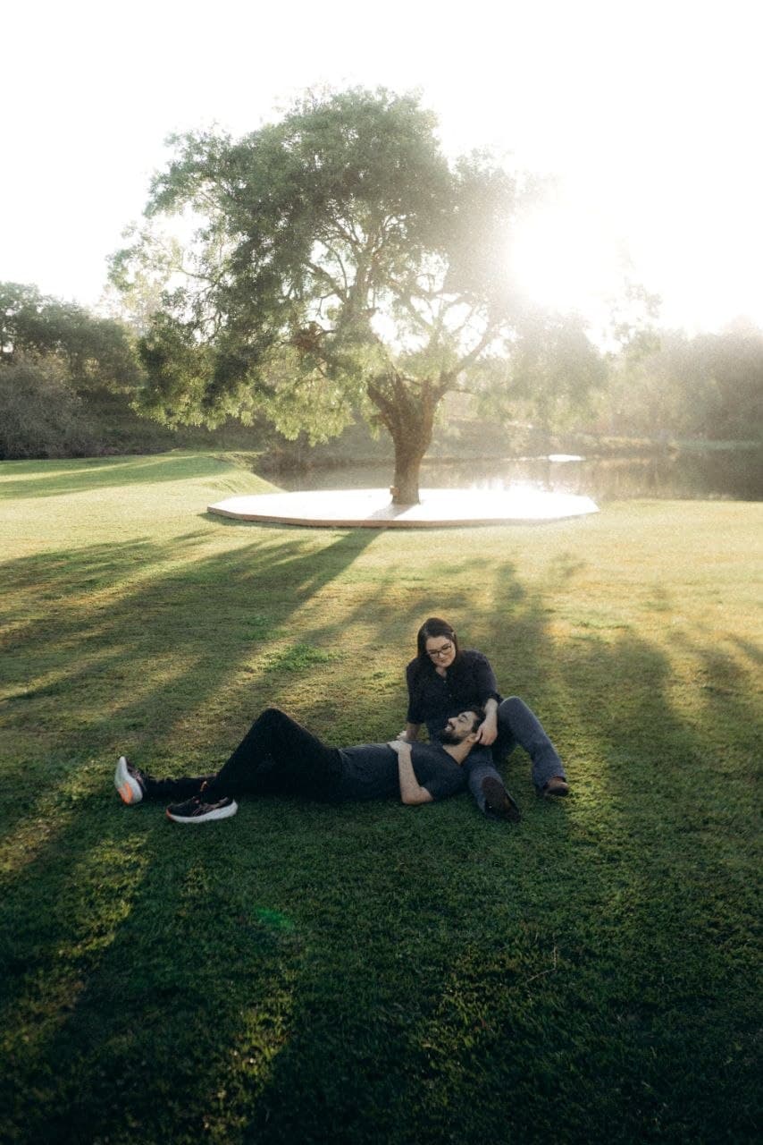 Camila e Bernardo descansando juntos na grama sob uma grande árvore